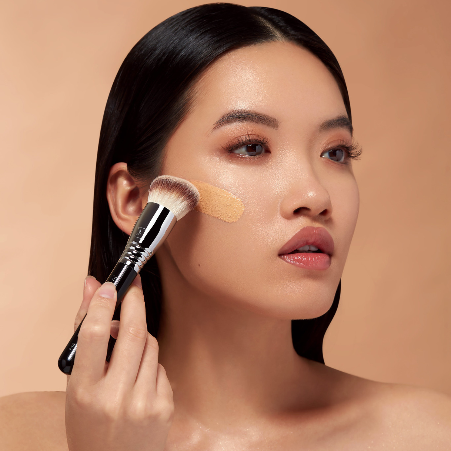 Woman applying skin tint with a Sigma Beauty makeup brush